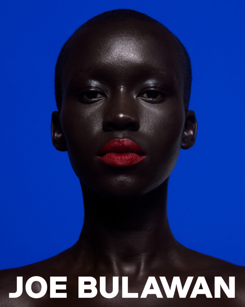 Beauty portrait of a model with deep skin tone and red lips, photographed against a rich blue background, part of Joe Bulawan’s branding.